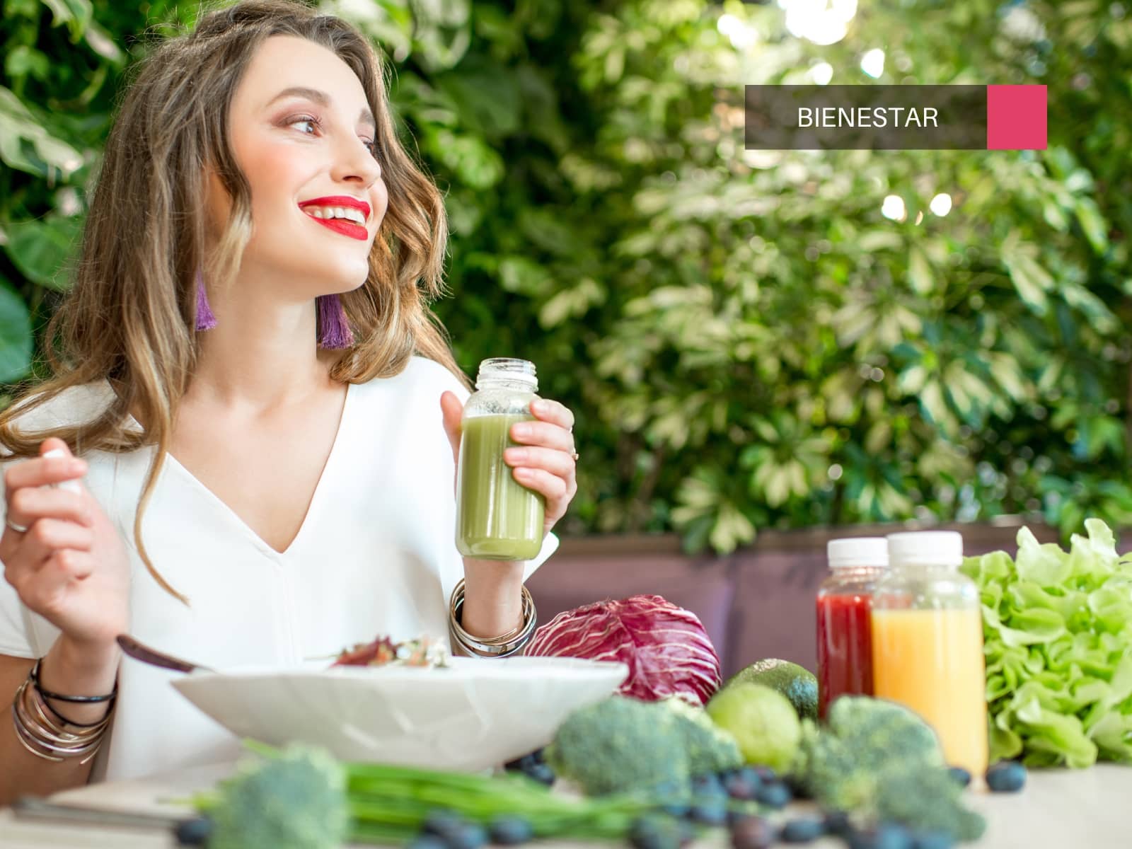 Mujer sonriente junto a una variedad de alimentos vegetales.