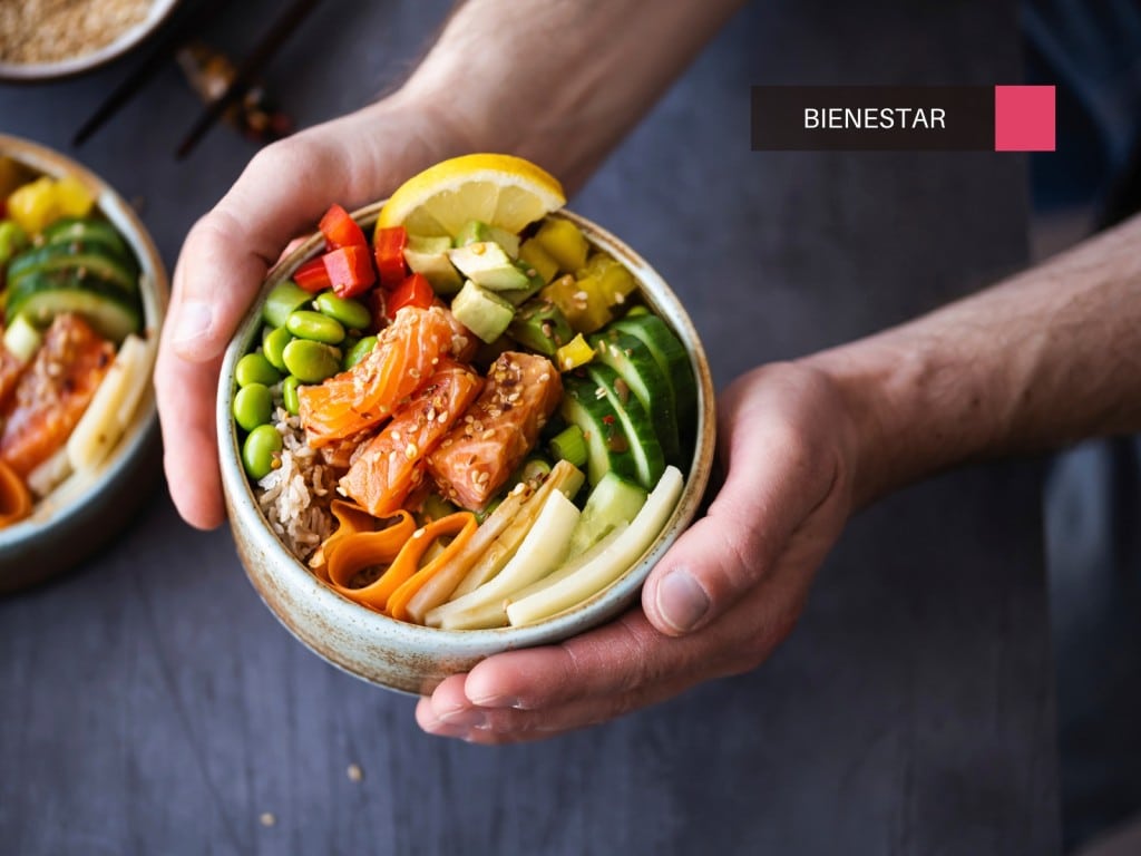 Manos sostienen un cuenco con salmón y verduras