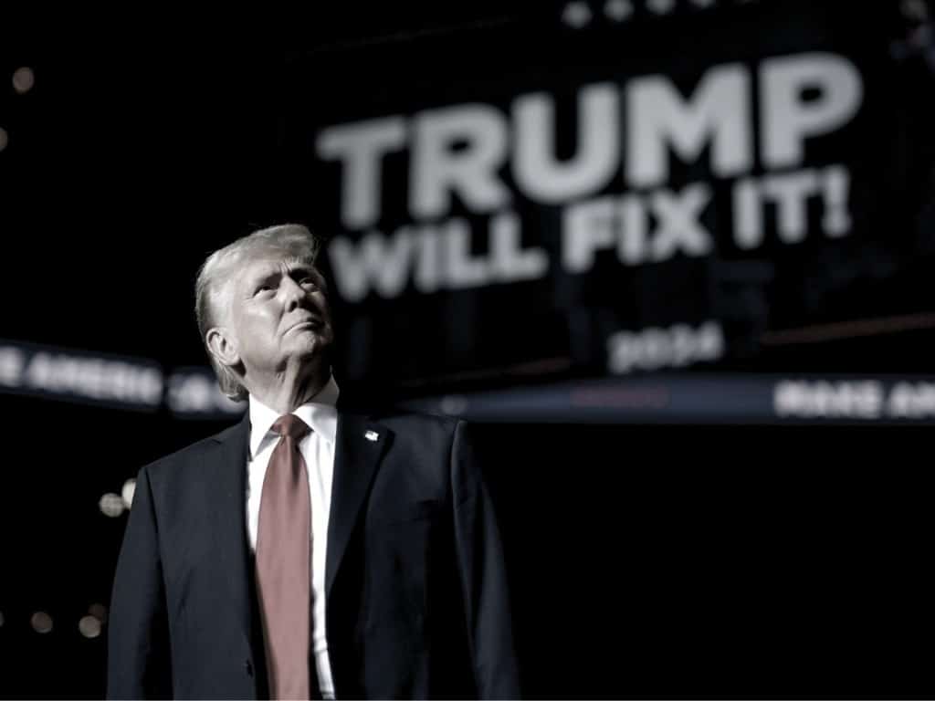 Donald Trump frente a pantalla que lee "Trump will fix it"