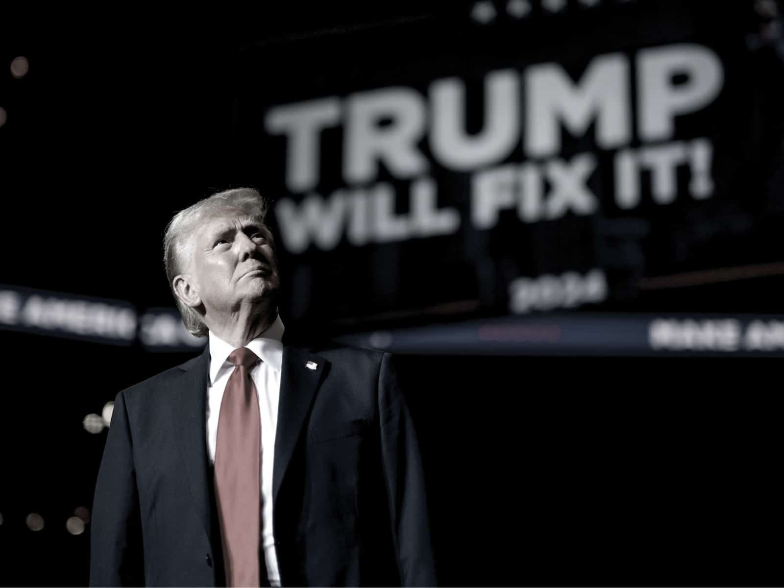 Donald Trump frente a pantalla que lee "Trump will fix it"
